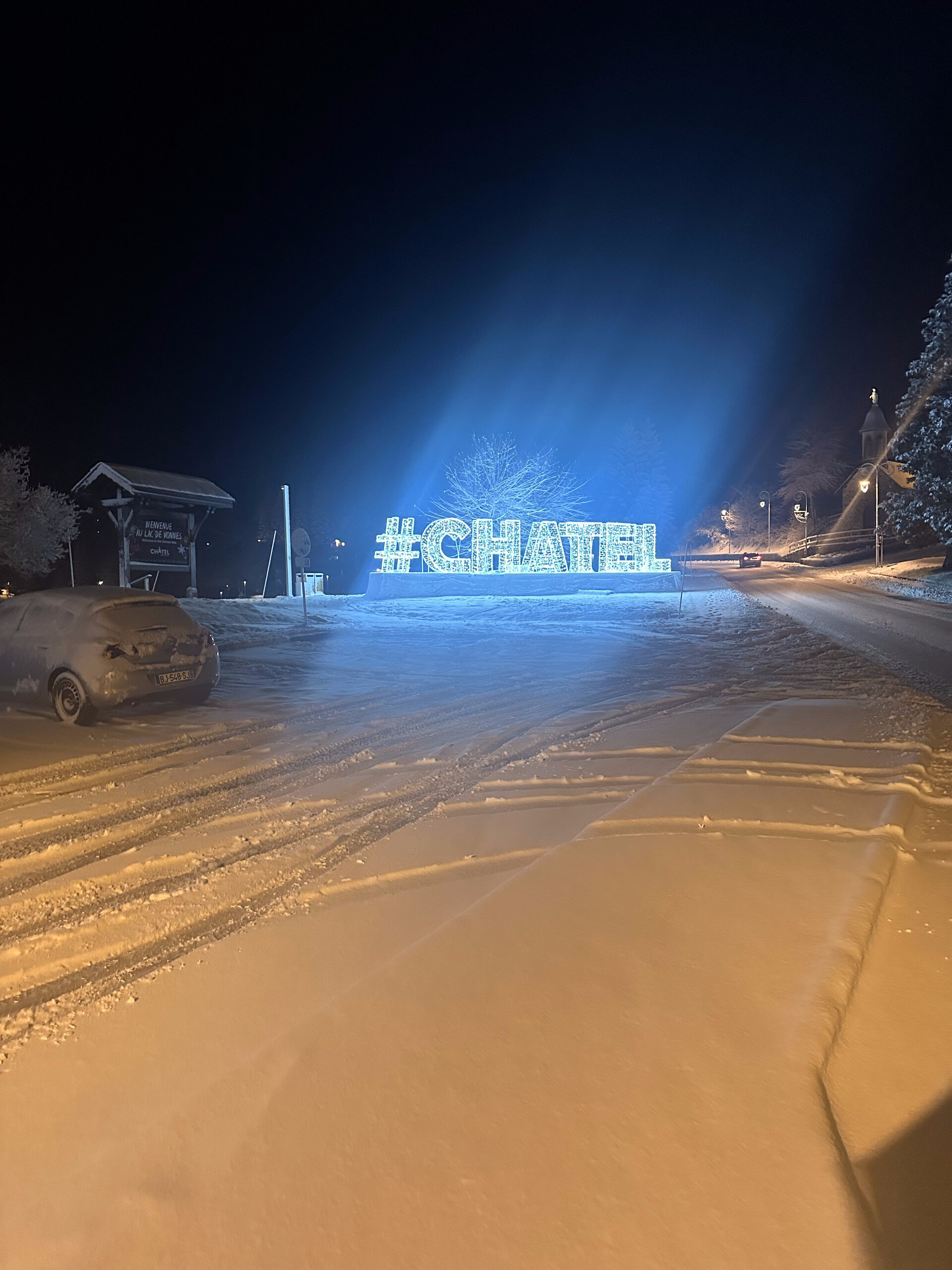 Illuminated #CHATEL sign on a snowy road near Lac de Vonnes at night